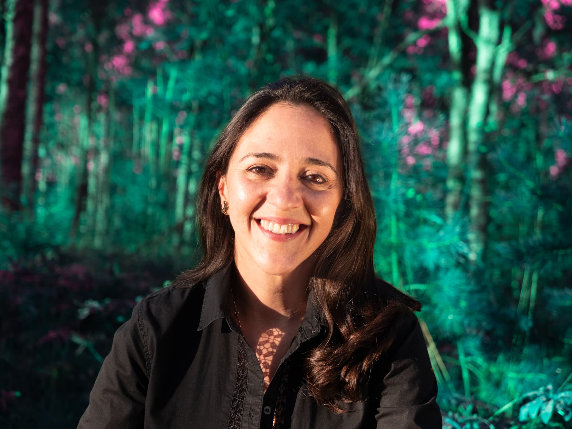 Marcela Campuzano standing in a forest, smiling against a backdrop of trees.
